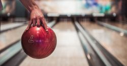 hand carrying a red bowling ball towards the bowling lane